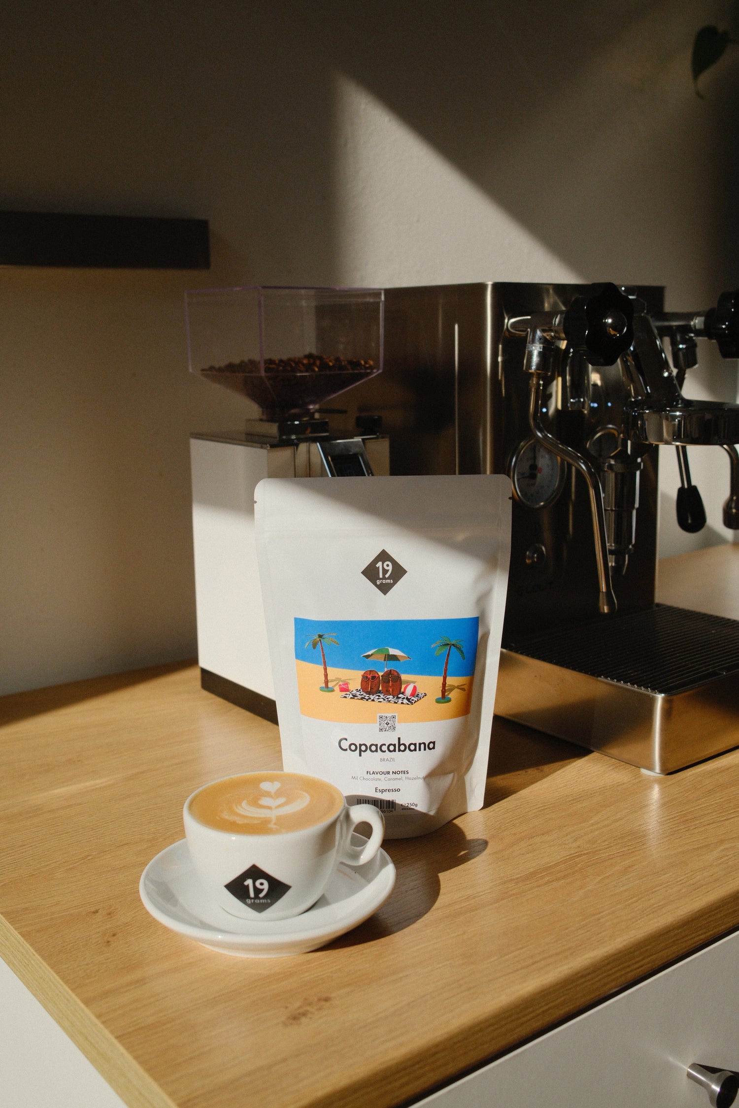 19grams Copacabana Brasilien Espresso Kaffeebeutel mit Cappuccino auf Holztheke – Specialty Coffee Lifestyle Flat Lay, Siebträgermaschine, Kaffeerösterei Berlin