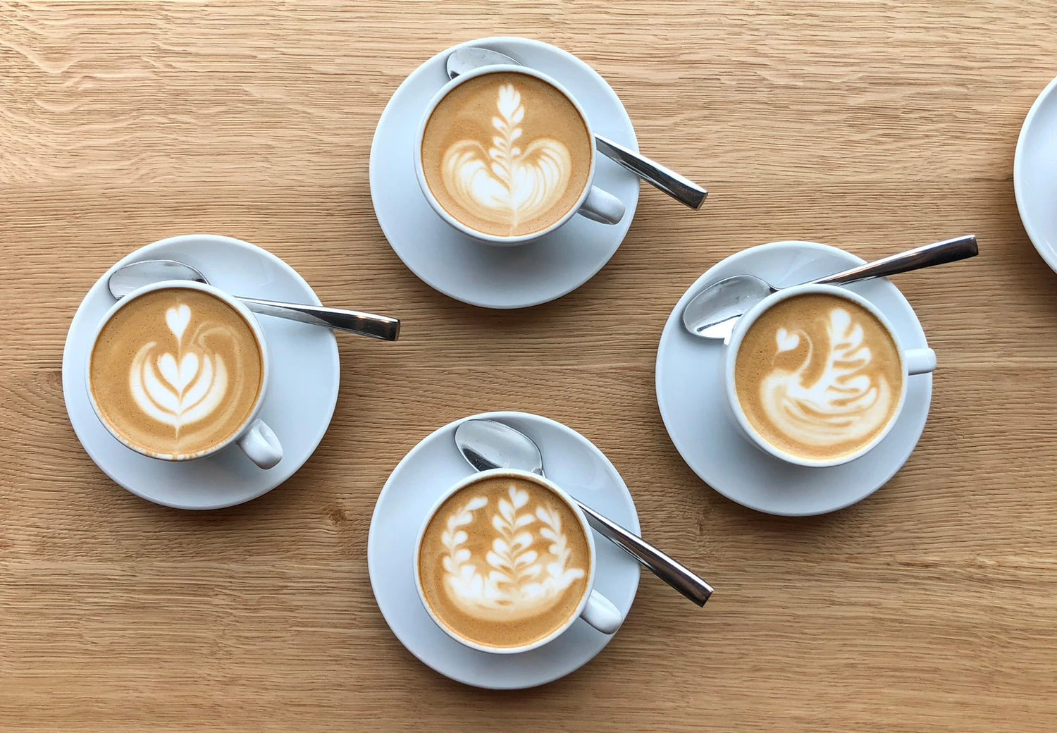 Vier Latte Art Tassen mit verschiedenen Mustern von oben – Latte Art Kaffeespezialitäten bei 19grams.live Roasters Berlin