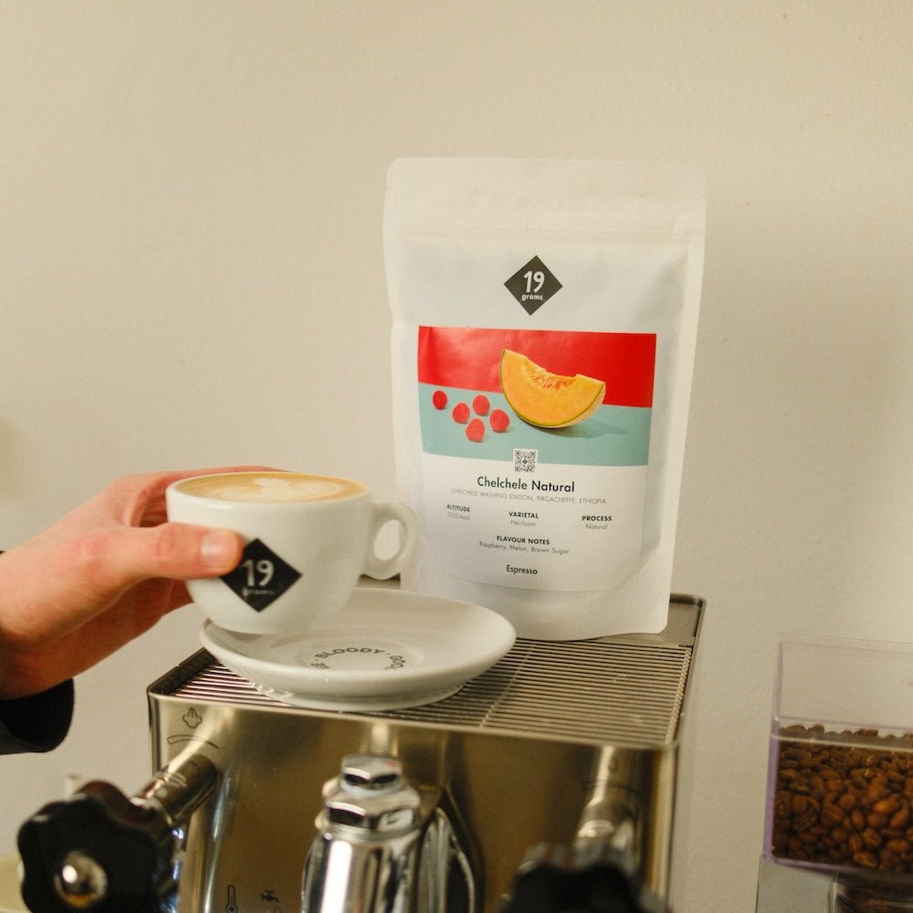 19grams Kaffeeverpackung Chelchele Natural Espresso aus Äthiopien auf einer Espressomaschine, daneben eine Cappuccinotasse