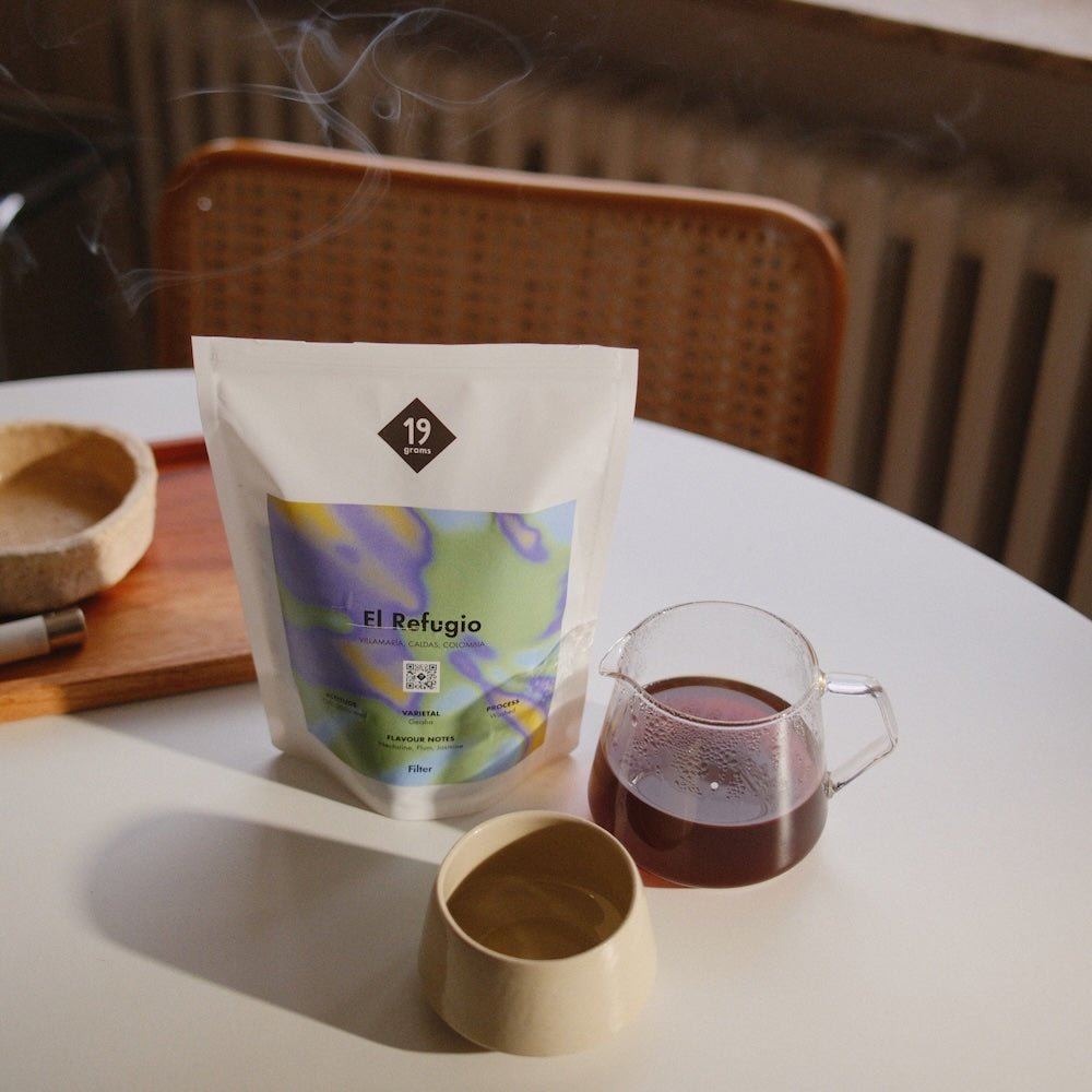 19grams „El Refugio" Kolumbien auf weißem Tisch neben Glaskanne mit Filterkaffee und Keramiktasse
