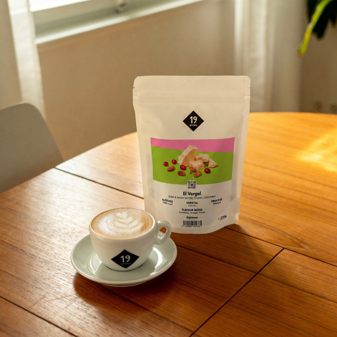 19grams El Vergel Specialty Coffee Espresso – Kaffeebeutel neben Cappuccino mit Latte Art auf Holztisch, Single Origin aus Kolumbien, Kaffeerösterei Berlin