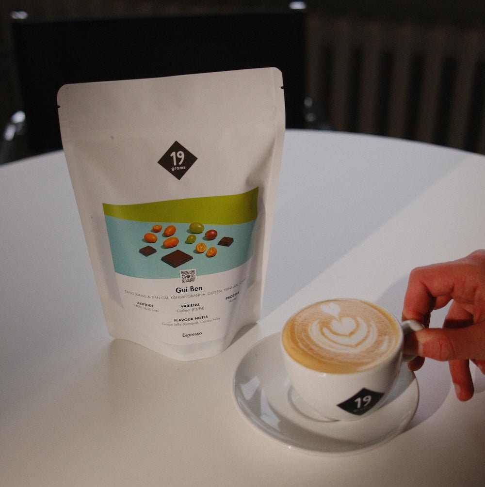 19grams Kaffeeverpackung „Gui Ben" Espresso aus China neben einem Cappuccino mit Latte Art auf weißem Tisch