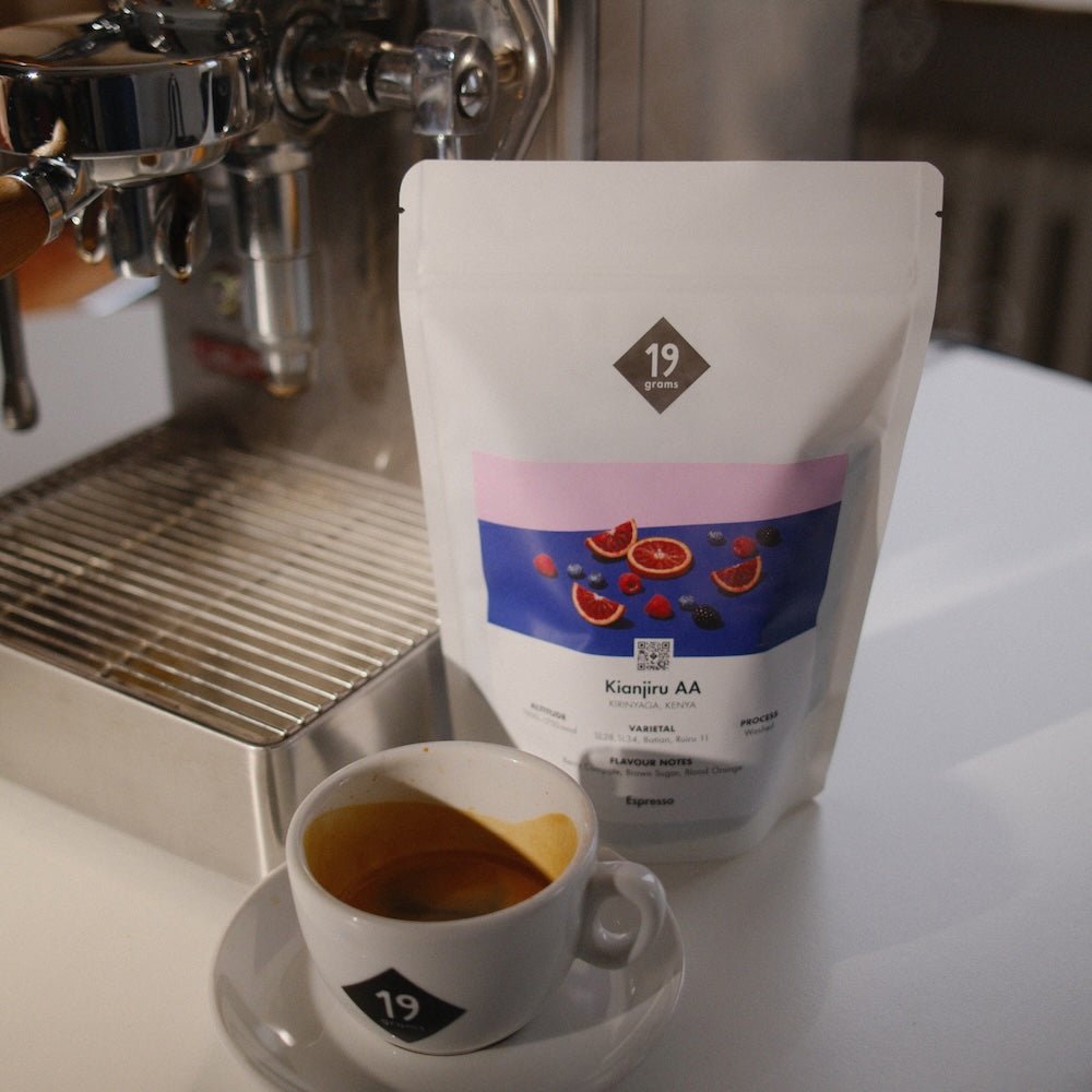 19grams Kaffeeverpackung Kianjiru AA Espresso aus Kenia vor einer Espressomaschine mit 19grams-Tasse – Produktfoto