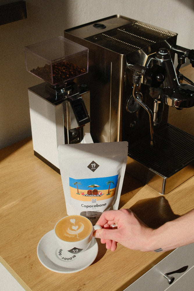 19grams Copacabana Brasilien Espresso Kaffeebeutel mit Cappuccino an Siebträgermaschine – Specialty Coffee Lifestyle-Foto, Hand hält Tasse, Kaffeerösterei Berlin