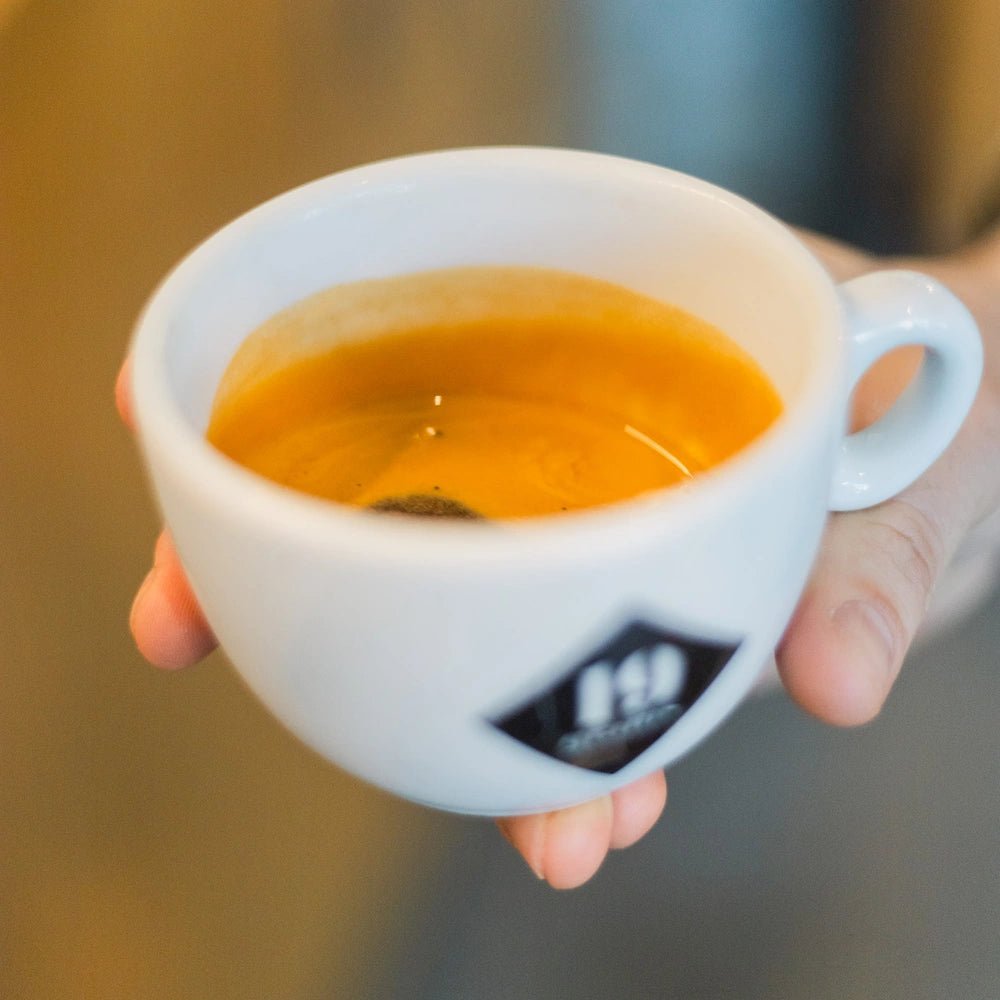 Hand hält 19grams Espressotasse mit frisch gezogenem Espresso – Barista-Training Espresso Kurs mit Arundhati Shenoy bei 19grams Specialty Coffee Roasters Berlin