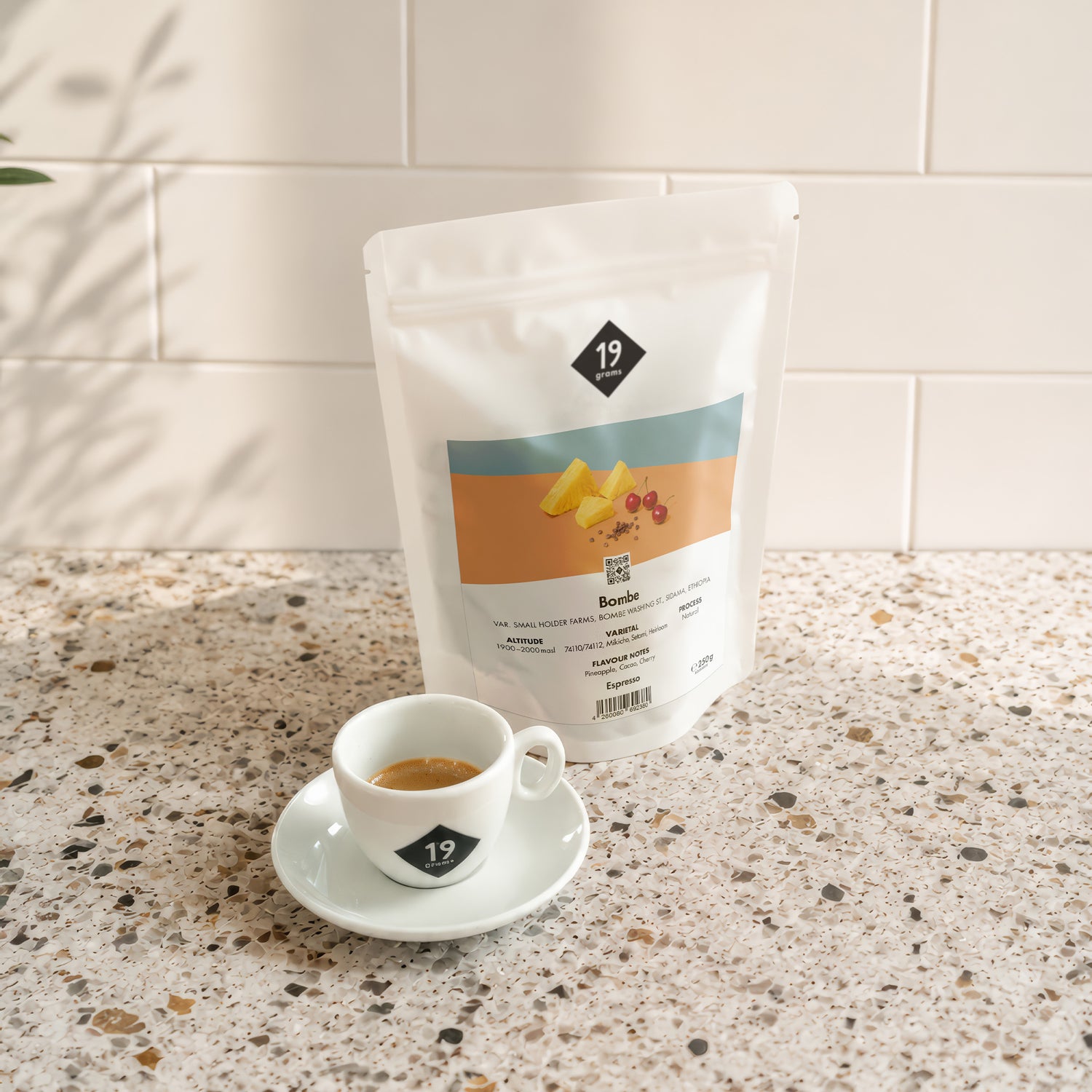 19grams Bombe Specialty Coffee Espresso – Kaffeebeutel neben frisch zubereitetem Espresso auf Terrazzo-Arbeitsplatte, Kaffeerösterei Berlin