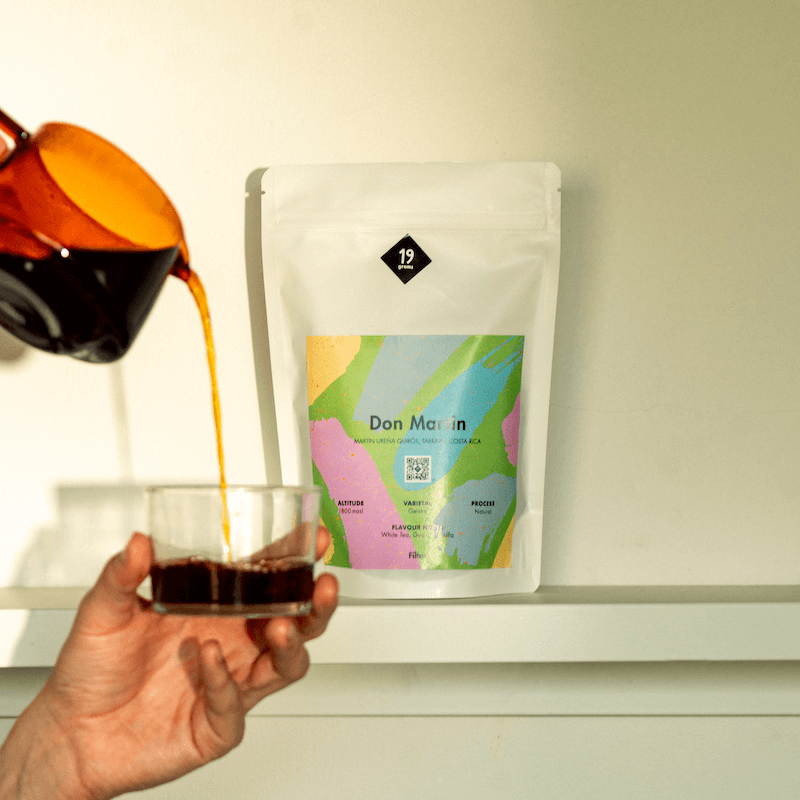 19grams Don Martin Geisha Natural Filterkaffee aus Costa Rica – Kaffeebeutel auf Regal mit frisch gebrautem Kaffee in der Tasse
