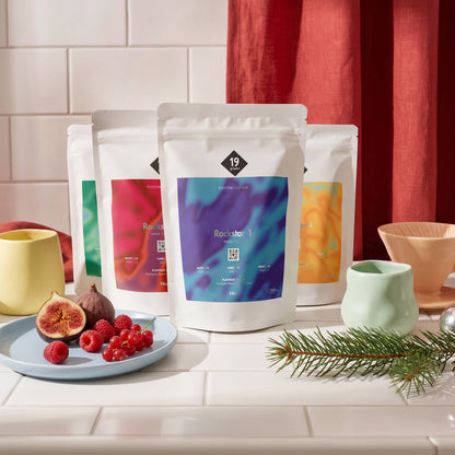 19grams Rockstar Calendar Specialty Coffee Moodbild – Bunte 19grams Kaffeebeutel mit Handfilter, Tasse, Feigen und Beeren auf Küchenfliesen, Kaffeerösterei Berlin