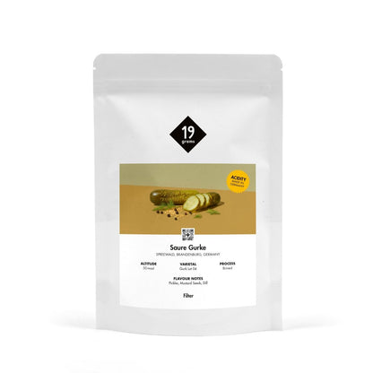 Produktmockup der 19grams Kaffeeverpackung „Saure Gurke" mit olivgrüner Banderole und Gurkenmotiv auf weißem Hintergrund