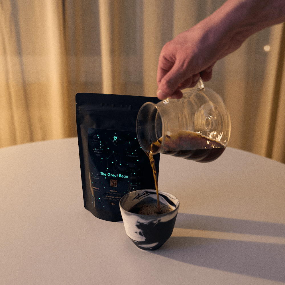 19grams „The Great Bean" – Filterkaffee aus Glaskanne in Keramiktasse, dunkle Verpackung mit Sternbild