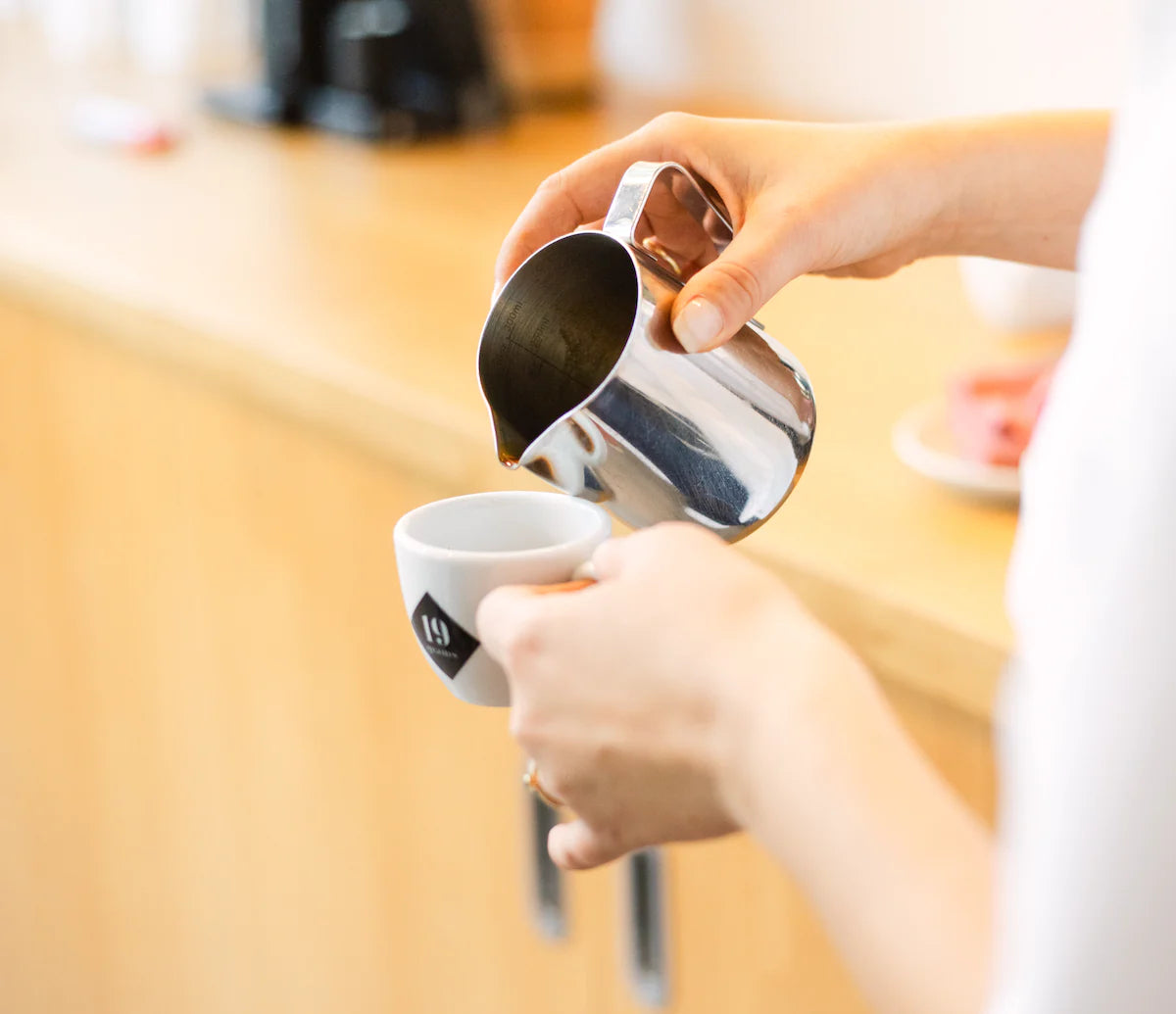 Barista gießt Milch in 19grams Espressotasse beim Workshop-Kurs Espresso Barista – Latte Art Technik beim Specialty Coffee Barista Workshop bei 19grams Berlin