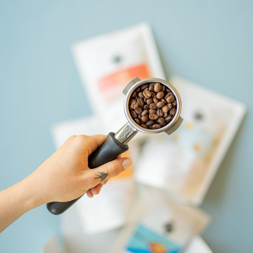 Siebträger gefüllt mit Kaffeebohnen im Hintergrund das 19grams Kaffeeprobier-Set
